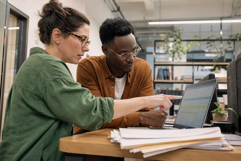 Sustainability analyst and accountant reviewing flagged invoice lines together on a laptop in a bright office