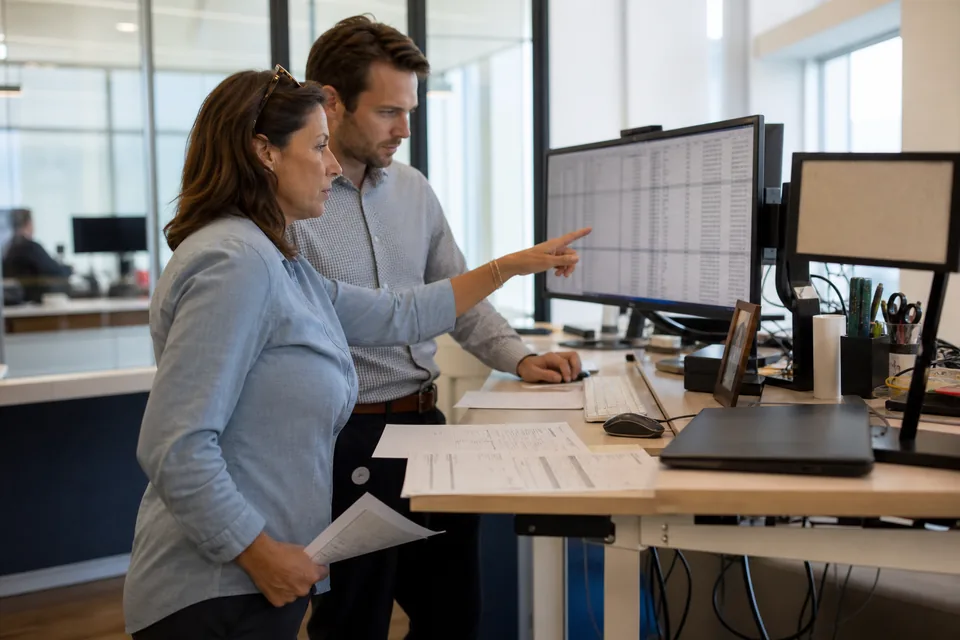 Controller and finance systems analyst reviewing accounts payable invoice lines on a large monitor in an office