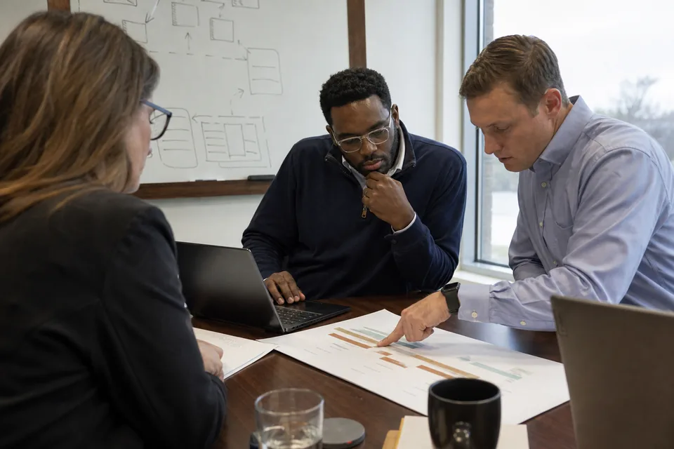 Sustainability manager, IT applications lead and CFO weighing an implementation plan around a meeting table