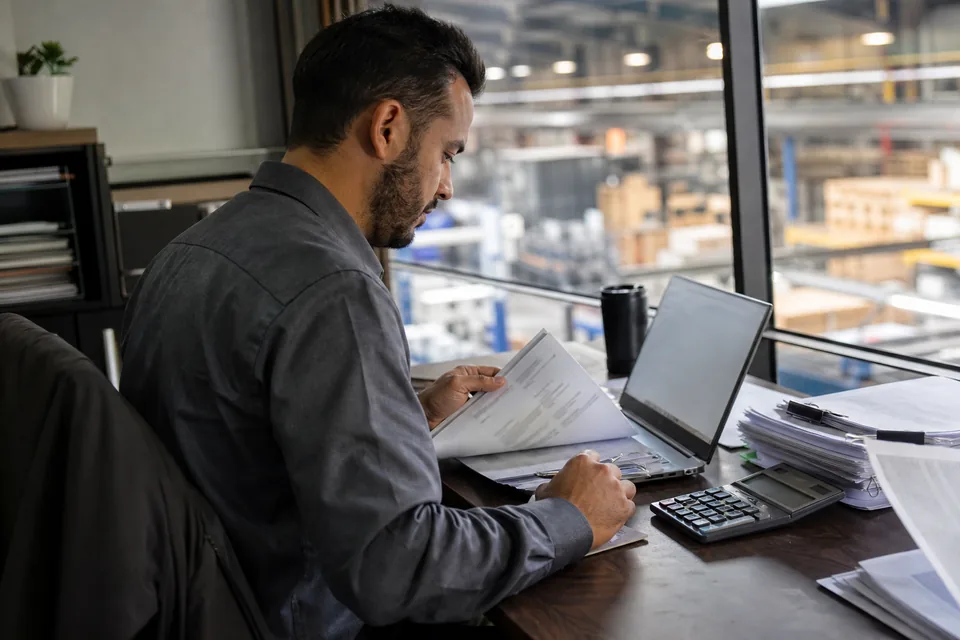 Finance operations manager at a desk with a laptop and supplier invoices in a manufacturing company office
